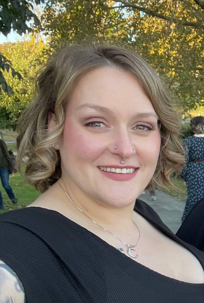 A photo of Jordan Magalis, electrologist. She is a white woman with shoulder length brown hair. She is wearing a black dress.